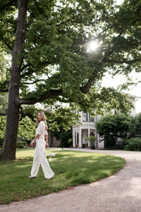 Woman wears cream LA LYNETTE pants, shown walking outdoors.