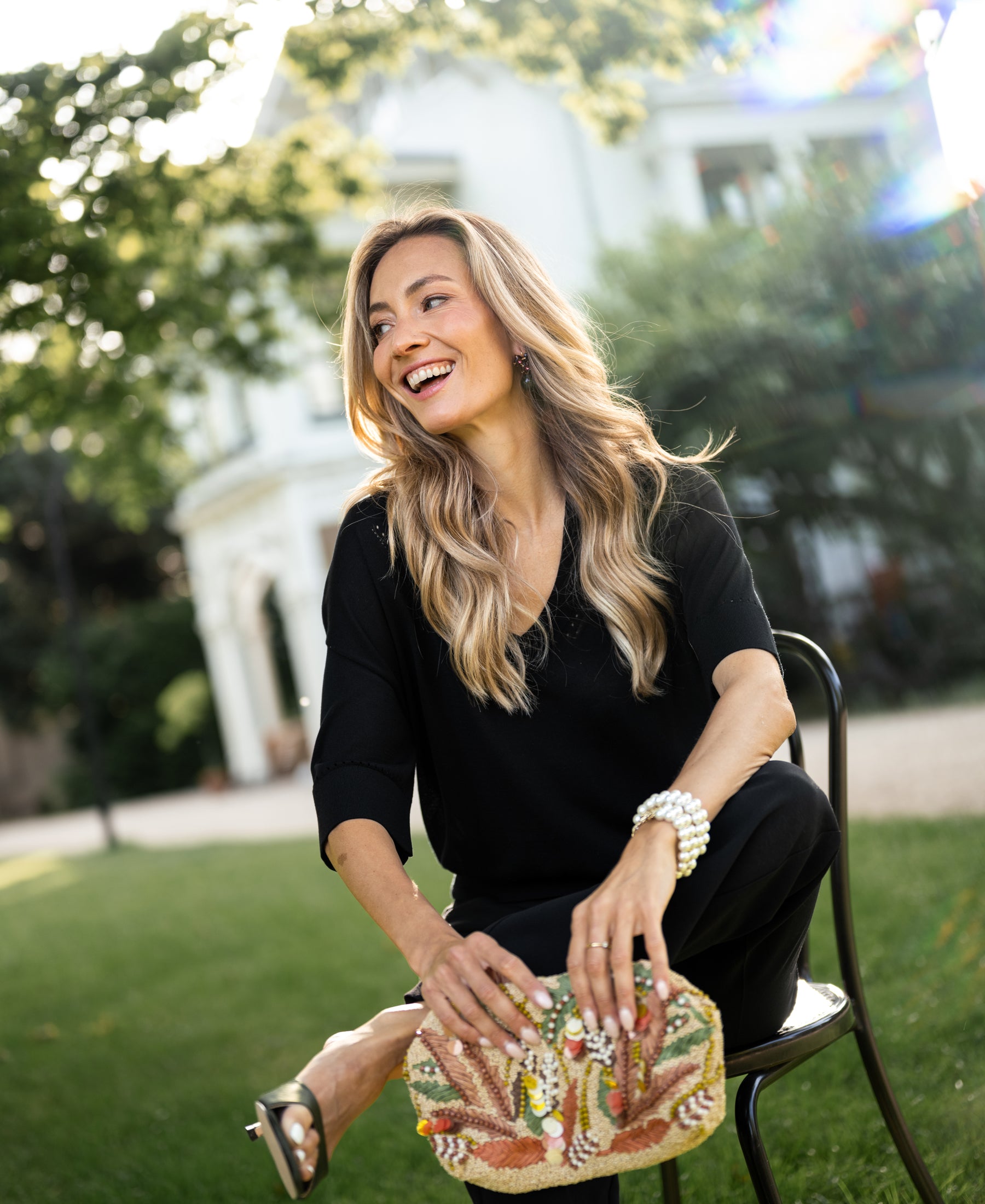 Woman wearing black silk LE MARDY top by PLEIN PUBLIQUE, seated outdoors.