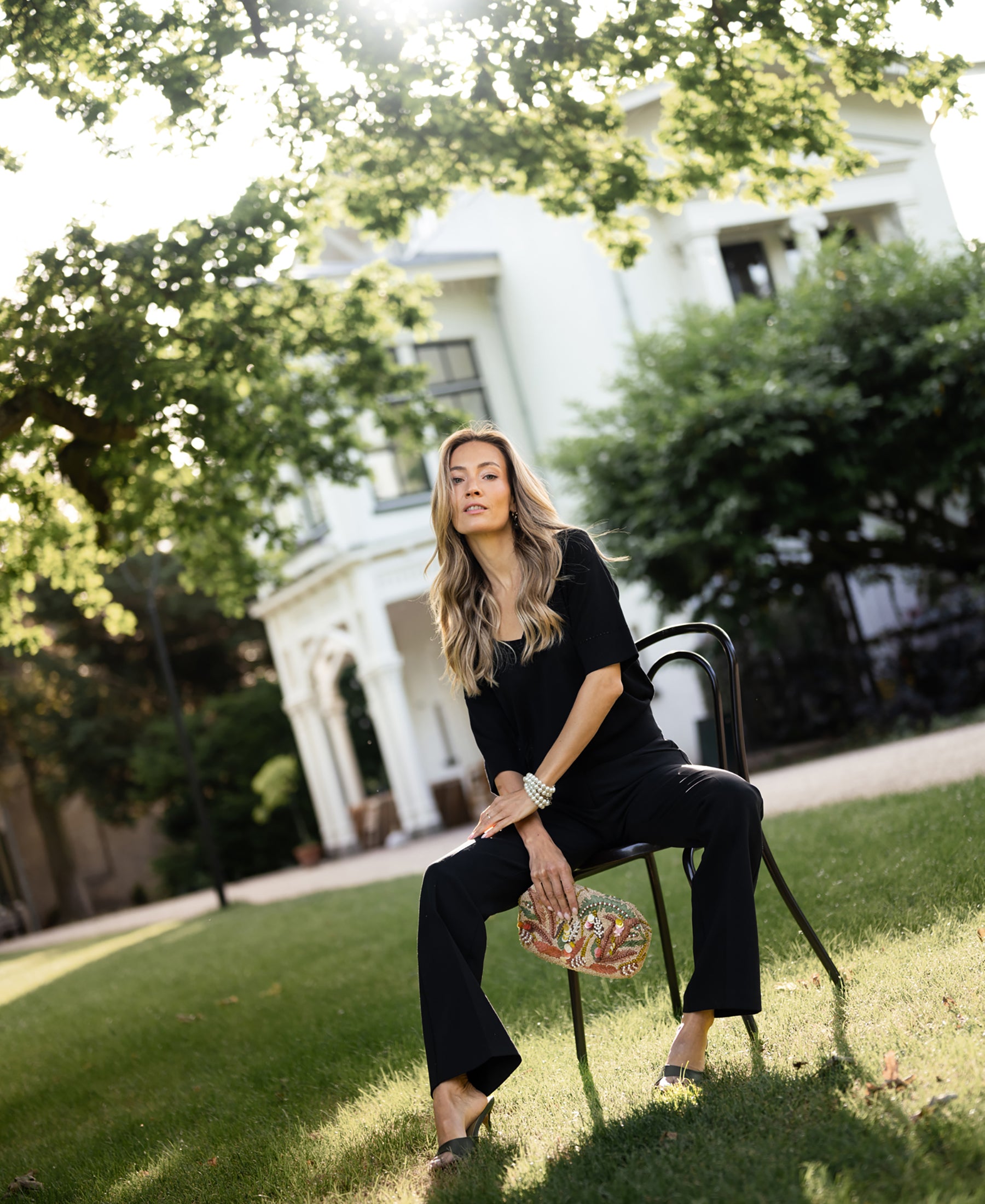 Woman wearing black LE MARDY silk top by PLEIN PUBLIQUE, seated outdoors.