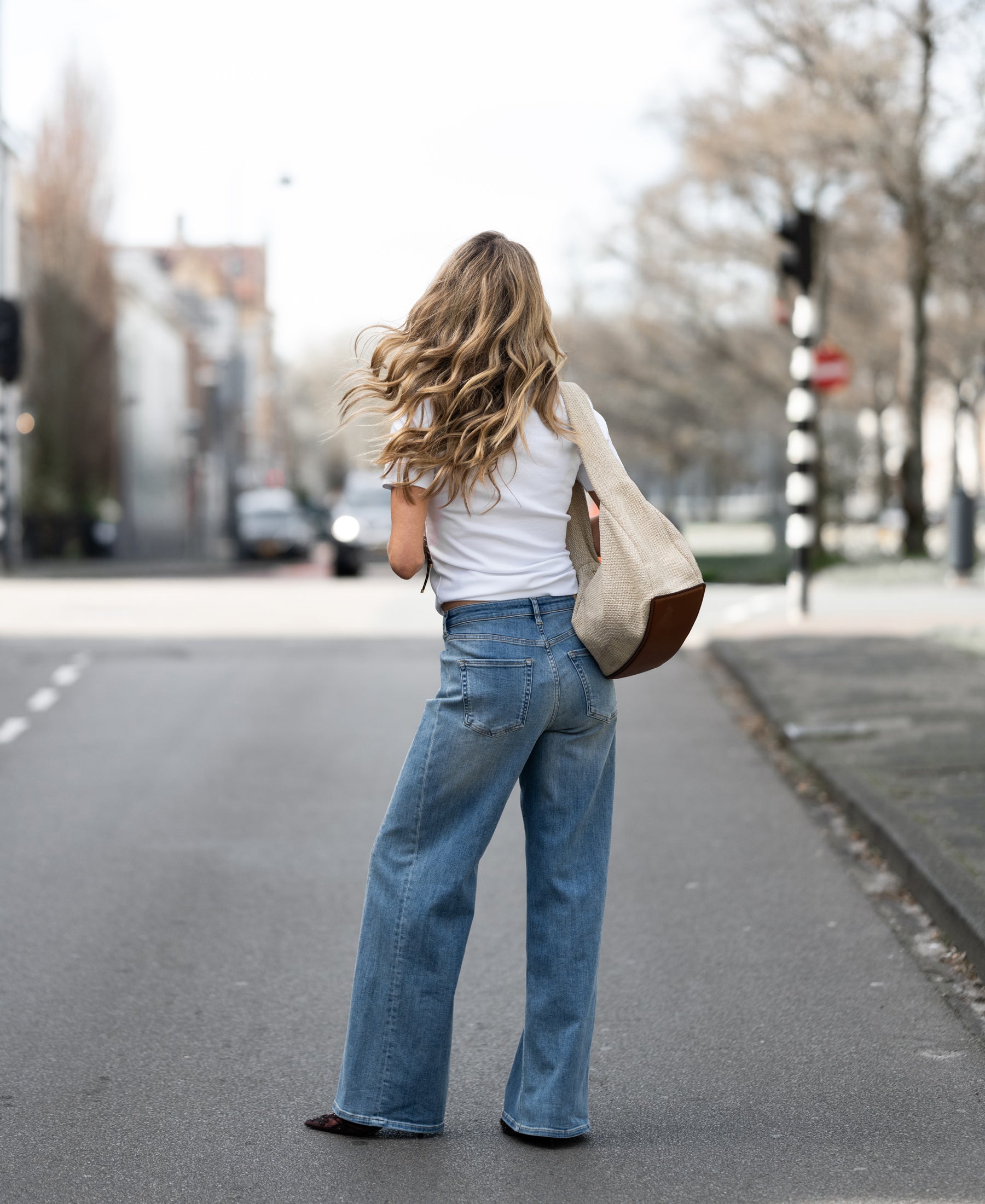 Wide leg jeans in light stone denim, shown worn by a woman standing on an empty street.