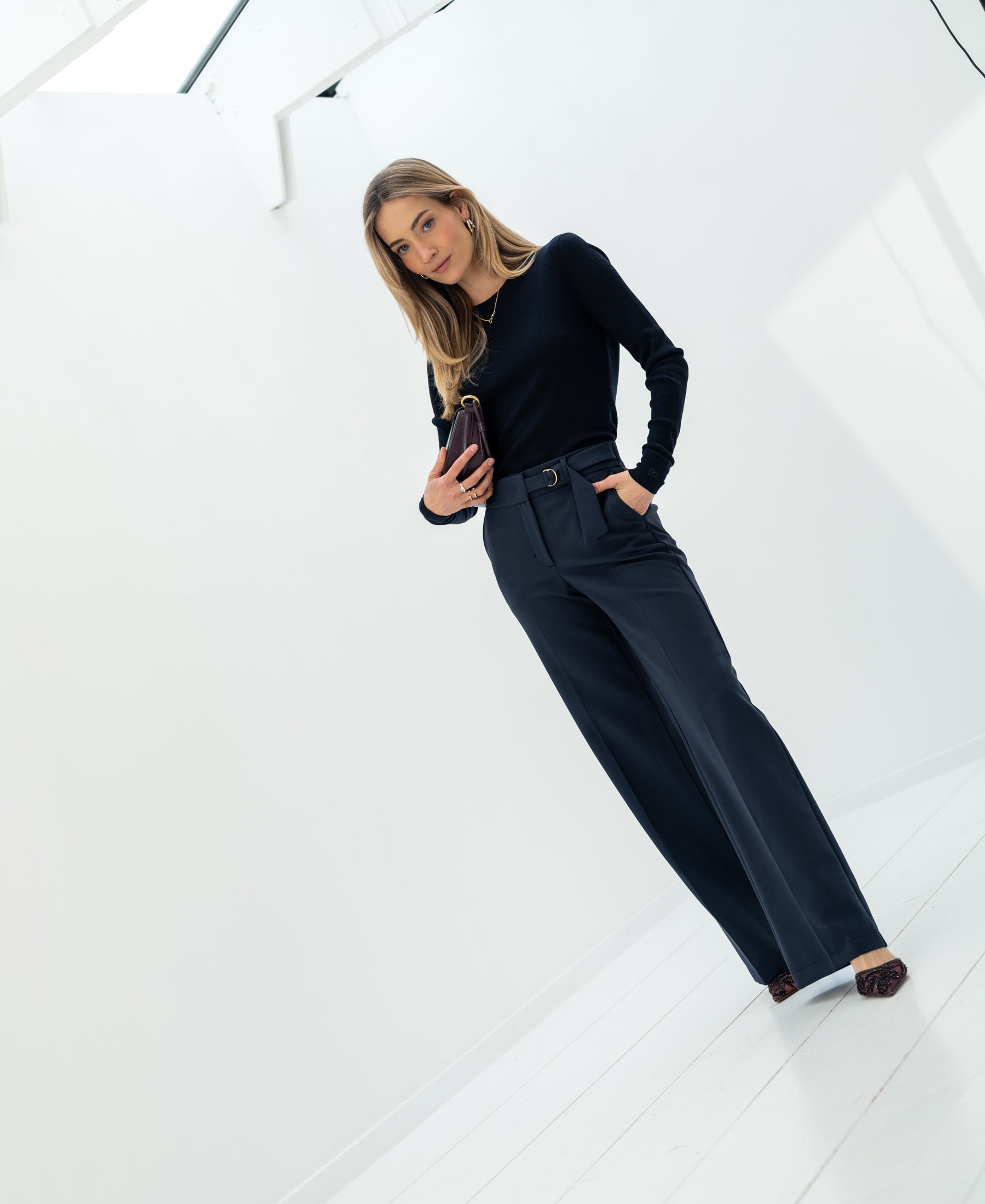 Woman wears luxury merino wool shirt in dark blue indoors, smiling.