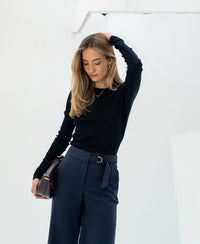 Woman wearing a PLEIN PUBLIQUE Luxe merino wool shirt in dark blue stands against a white background.