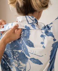 Close-up of a person fastening the collar of the LA MINOU floral print blouse with tie detail from PLEIN PUBLIQUE.