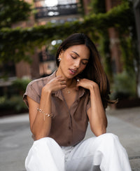 Woman wearing a mocha-colored cupro blouse outdoors, touching her hair.