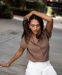 Woman wearing a mocha brown cupro blouse, seated on sidewalk with eyes closed.