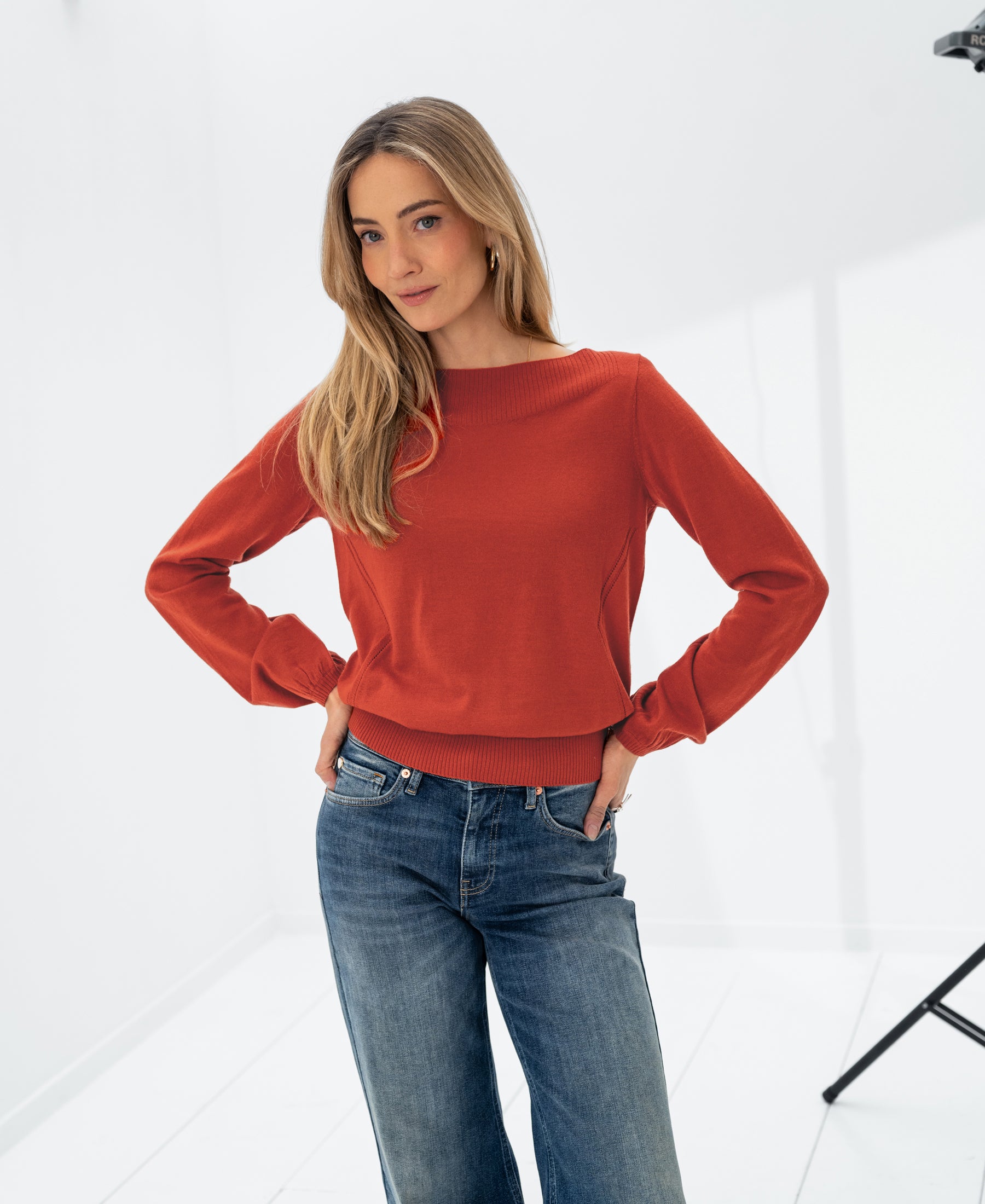Woman wearing LA MUSE Cayenne boatneck sweater by PLEIN PUBLIQUE poses in bright, white studio.