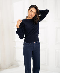 Woman wears the LA MUSE boatneck sweater by PLEIN PUBLIQUE in dark blue, standing indoors.
