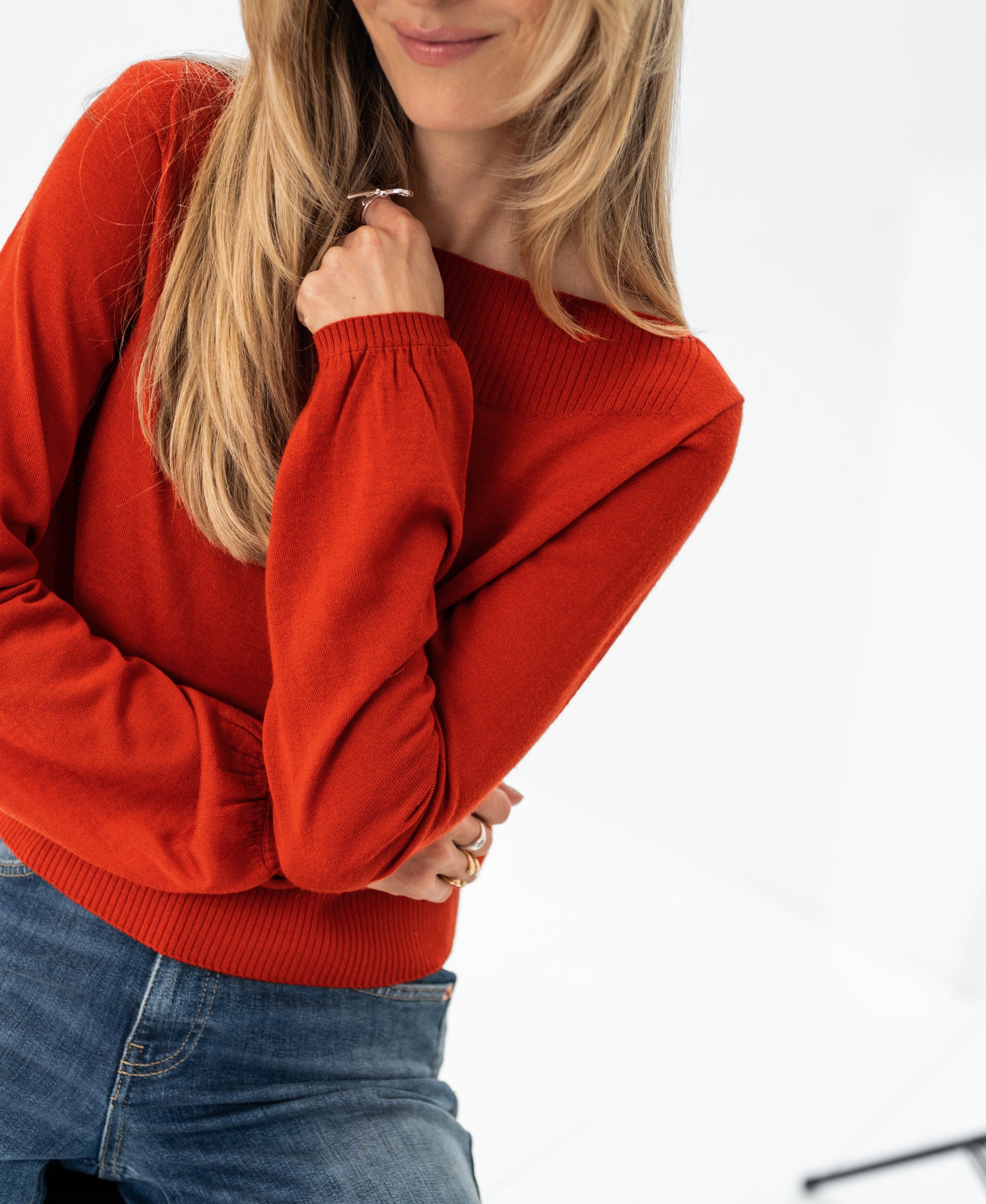 Woman wearing PLEIN PUBLIQUE LA MUSE boatneck sweater in Cayenne, standing and smiling against a white background.