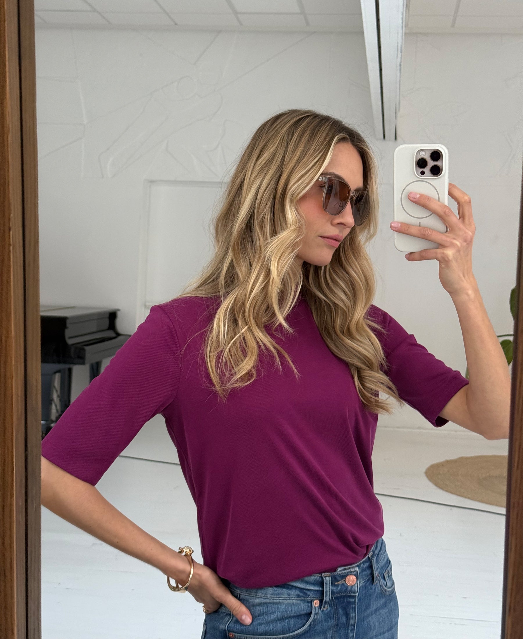 Woman wearing a magenta ribbed collar top takes a mirror selfie.