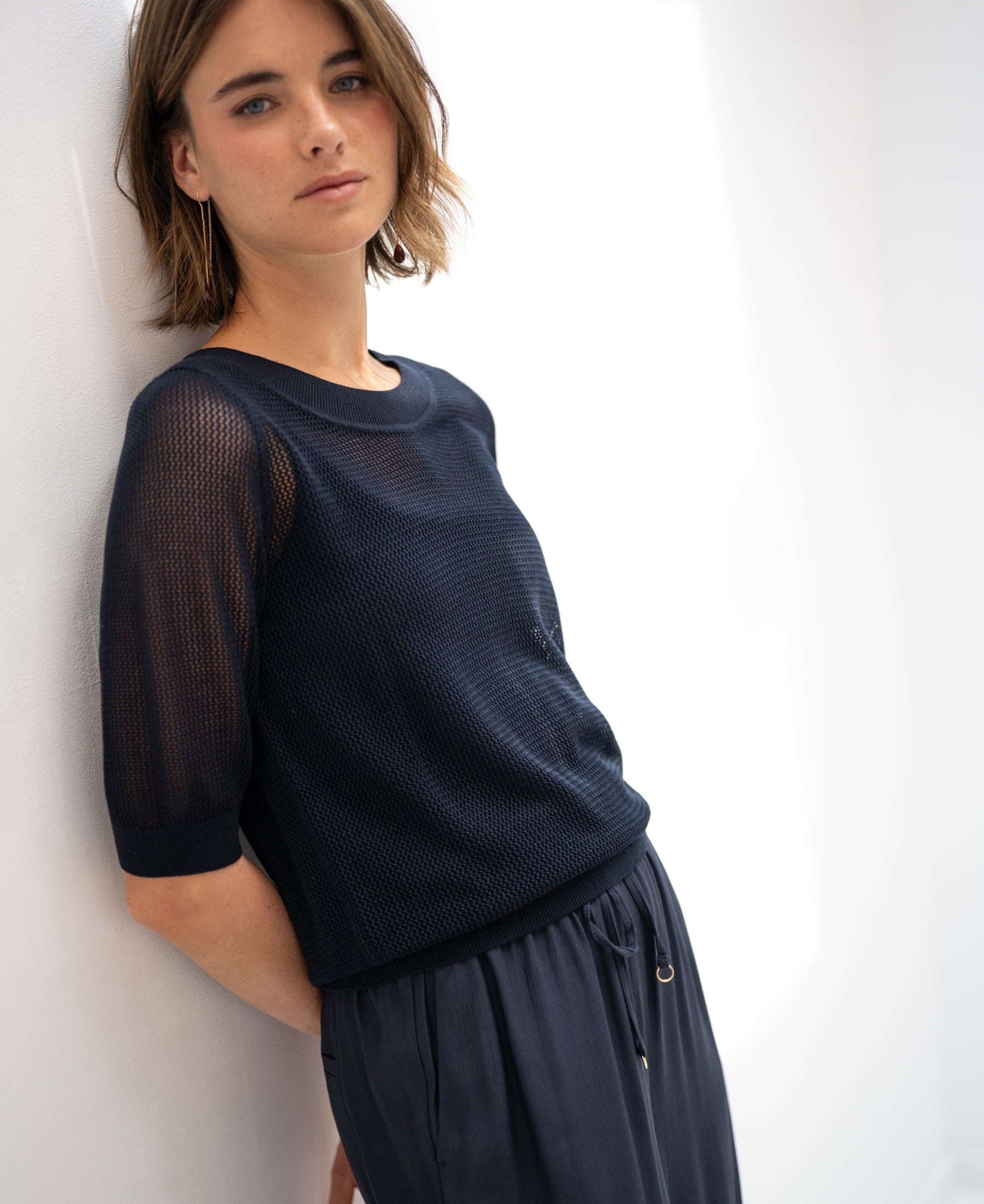 Dark blue mesh sweater with silk by PLEIN PUBLIQUE shown on a woman leaning against a white wall.