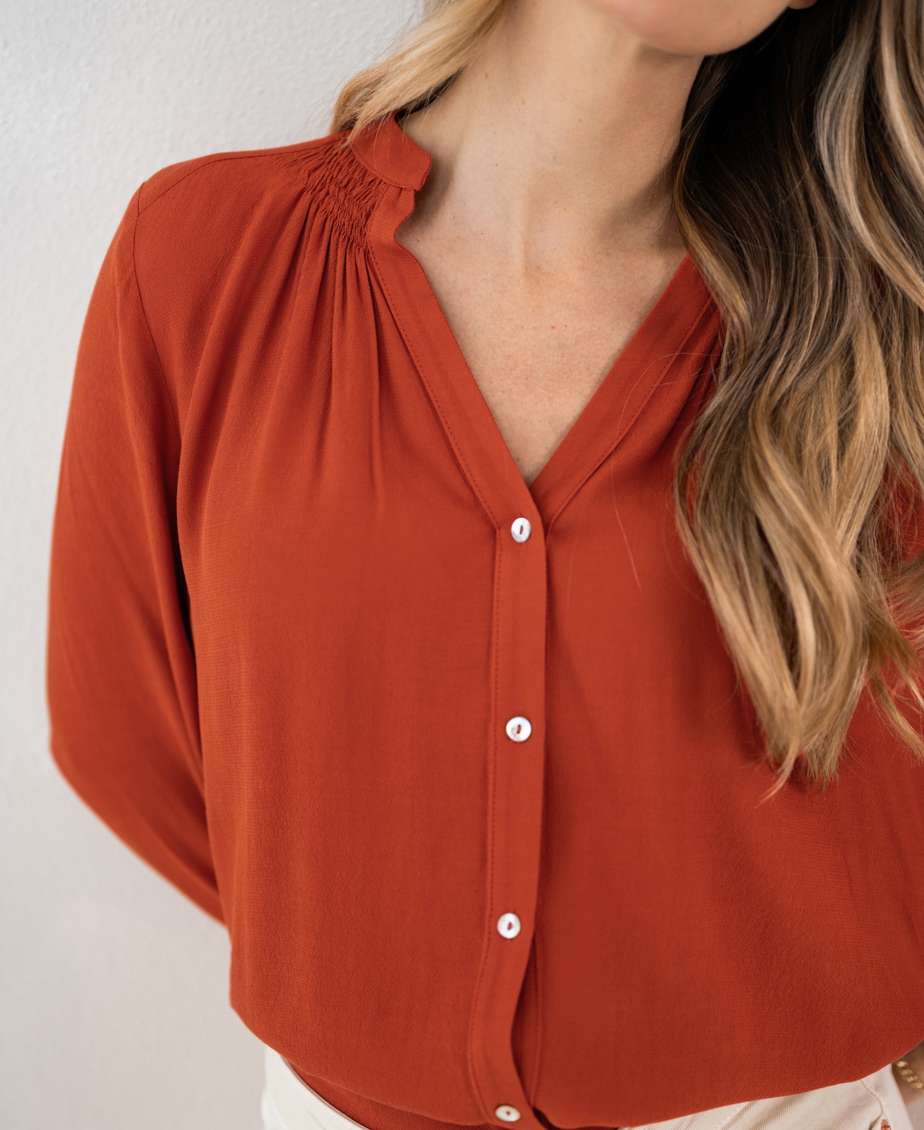 Burnt orange v-neck blouse, smocked shoulders, button-up front, viewed from the side.