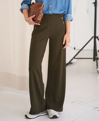 Dark olive green PLEIN PUBLIQUE travel pants, minimal bright background.