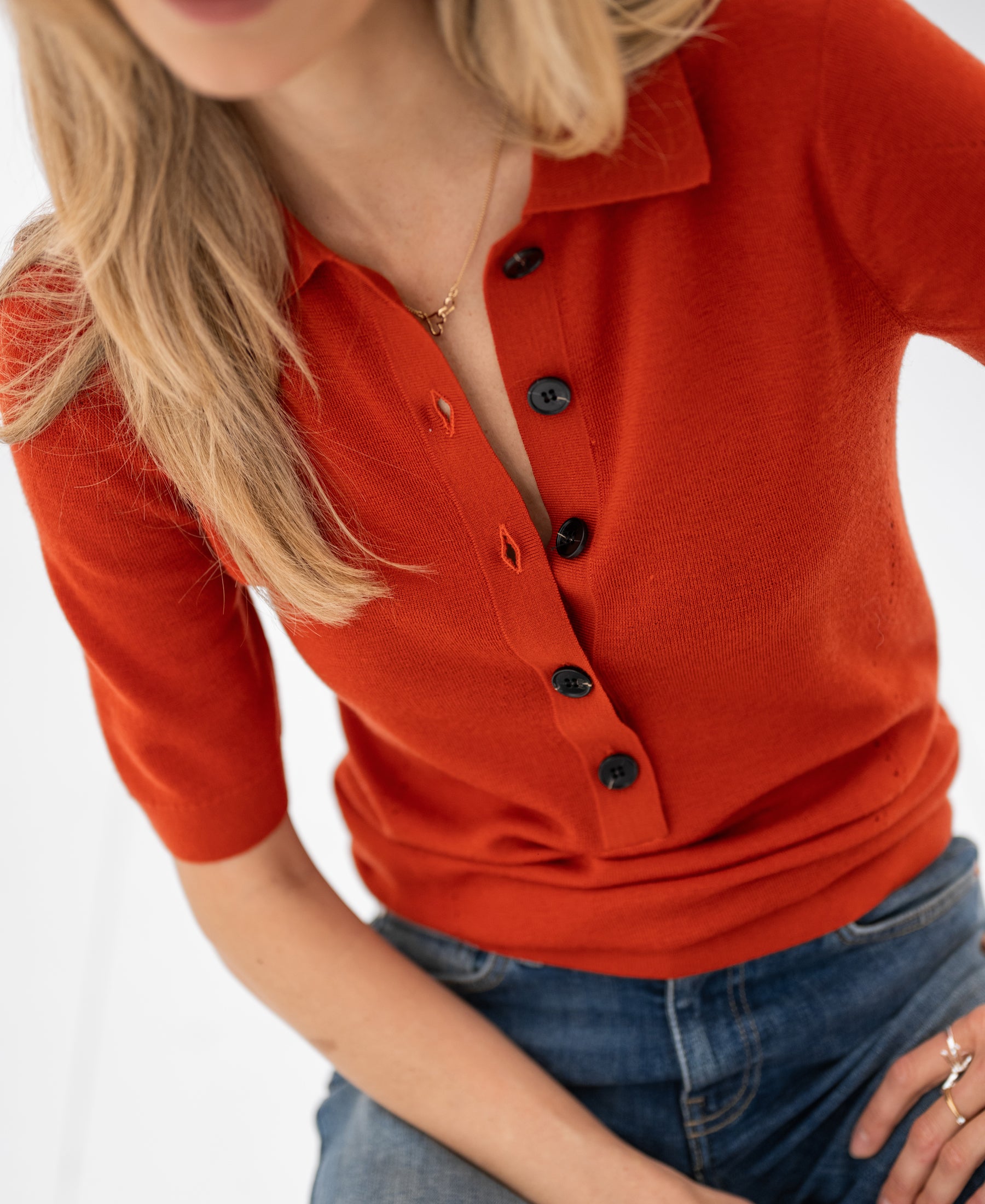 Woman wearing a merino wool polo sweater in cayenne red, seated with hair partly over face.