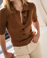 Camel-colored merino wool polo shirt by PLEIN PUBLIQUE LA PANTIN, shown indoors with sunlight streaming in.