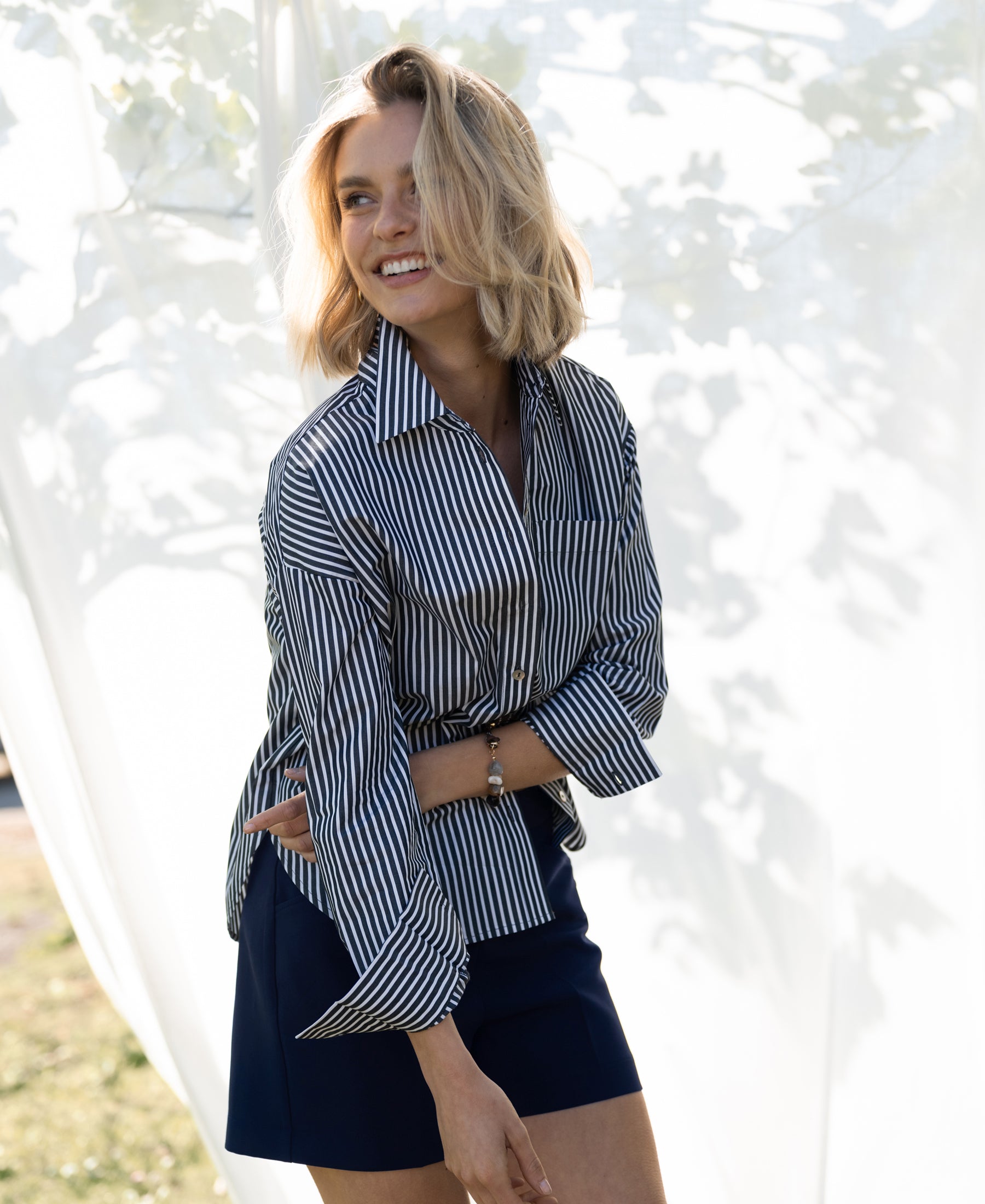 Striped white and anthracite blouse from LA PASCALLE, shown outdoors with sunlight filtering through leaves.