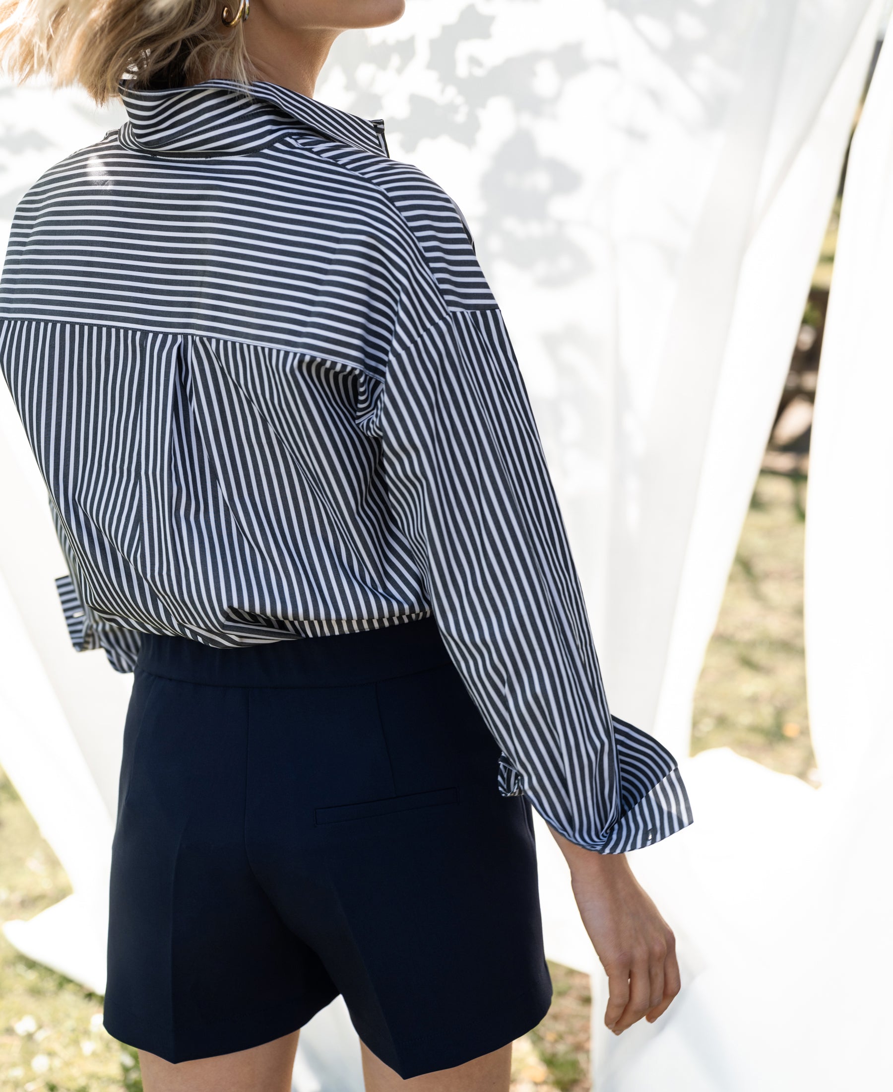 Woman wearing LA PASCALLE white-anthracite striped blouse, outdoors in sunlight with a light background.