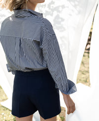 Woman wearing LA PASCALLE white-anthracite striped blouse, outdoors in sunlight with a light background.