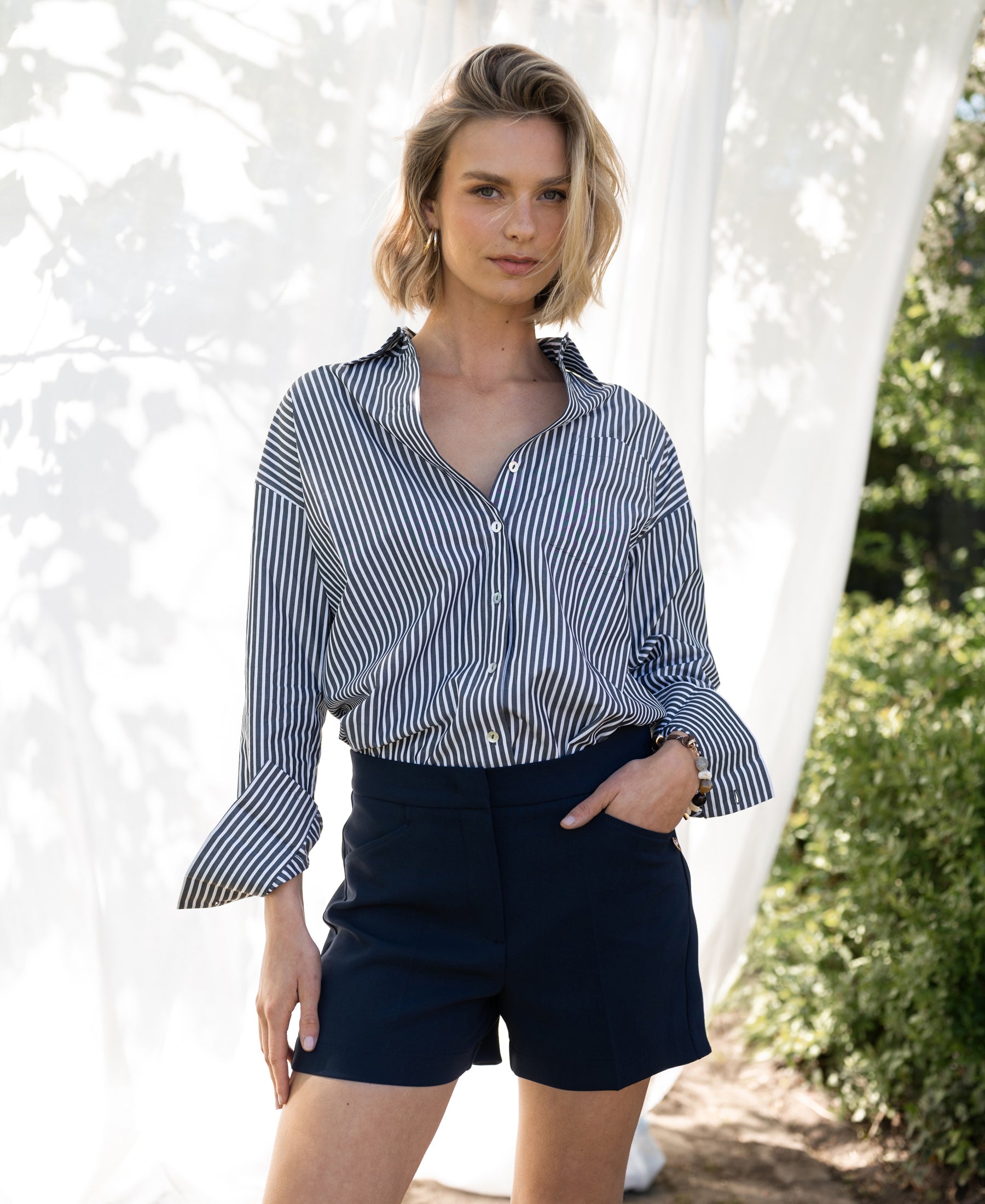 Woman wearing LA PASCALLE white-anthracite striped blouse, standing in sunlight with fabric billowing around her.