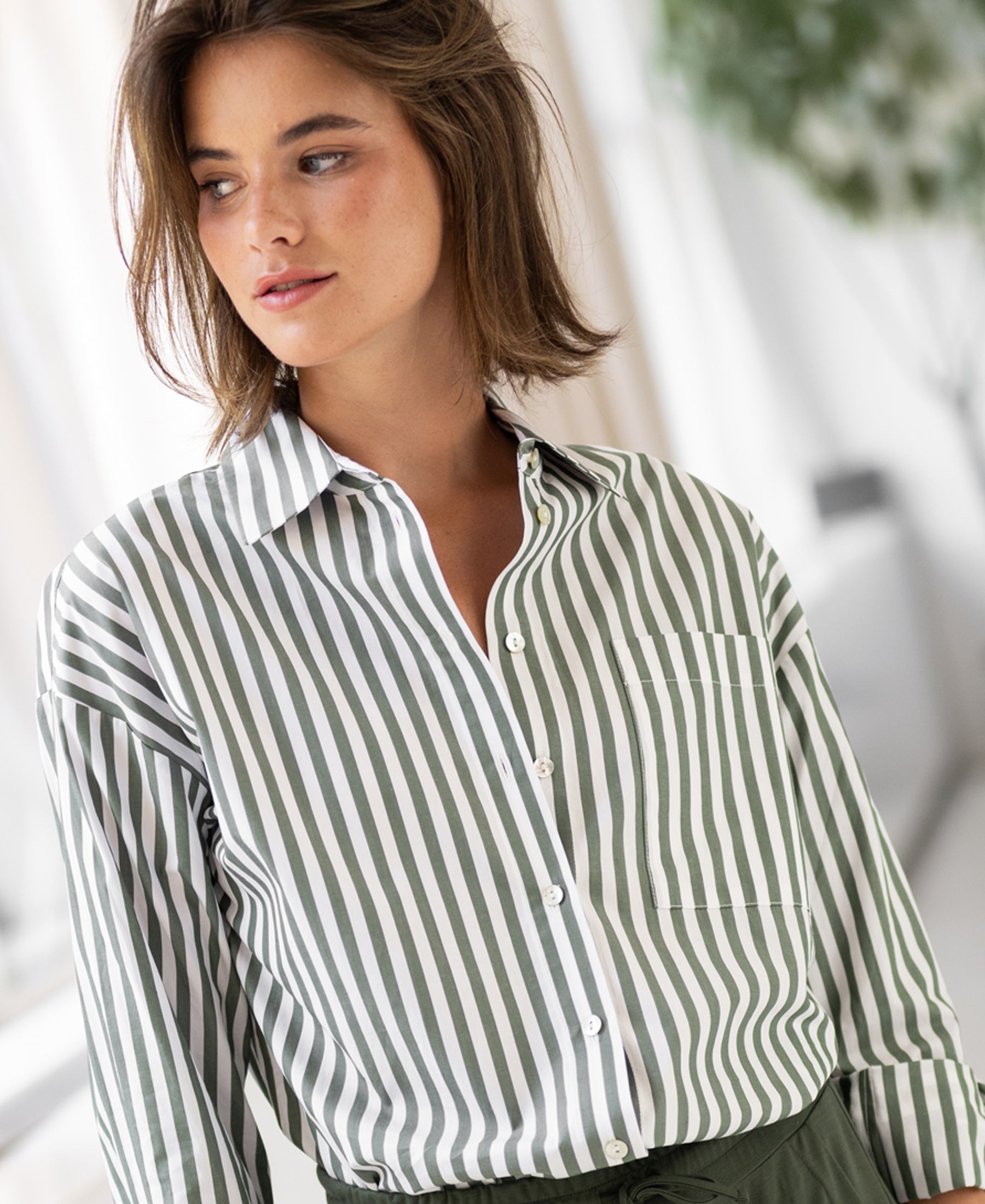 White and olive green striped blouse by Plein Publique La Pascale, shown indoors.