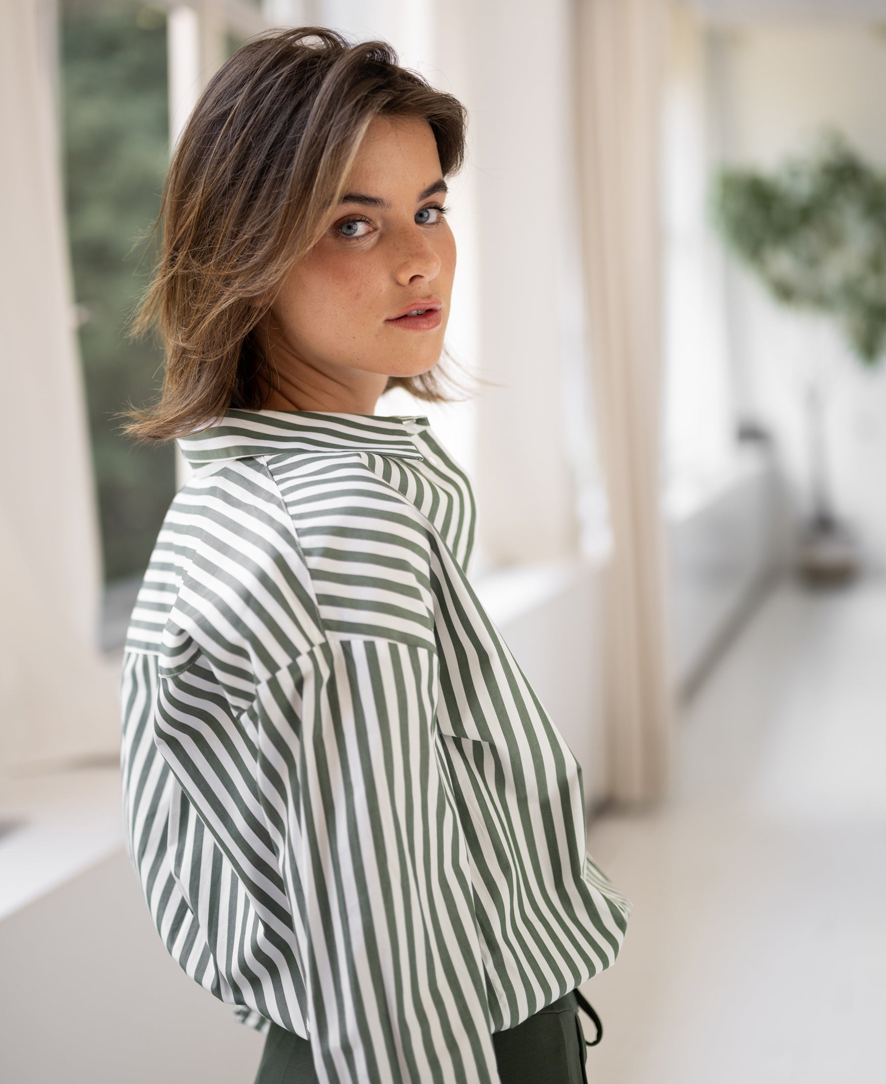Striped white and olive green blouse by PLEIN PUBLIQUE, model seen from the back, looking over her shoulder.