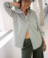 Woman wearing a PLEIN PUBLIQUE LA PASCALLE white and olive-green striped blouse indoors by a sunlit window.
