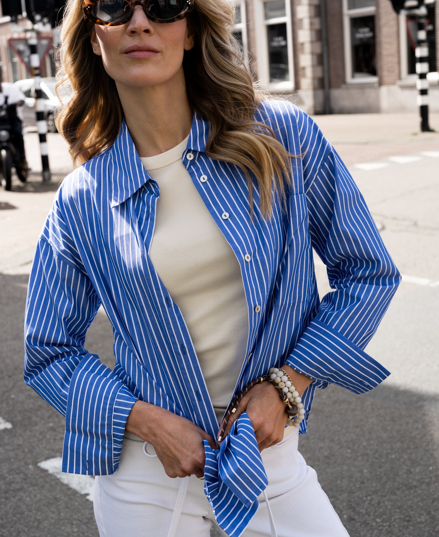 Blue-and-white striped PLEIN PUBLIQUE LA PASCALLE blouse with tied front, shown outdoors in sunlight.