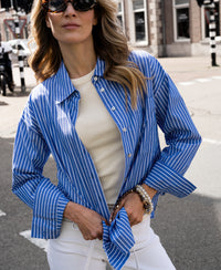 Blue-and-white striped PLEIN PUBLIQUE LA PASCALLE blouse with tied front, shown outdoors in sunlight.