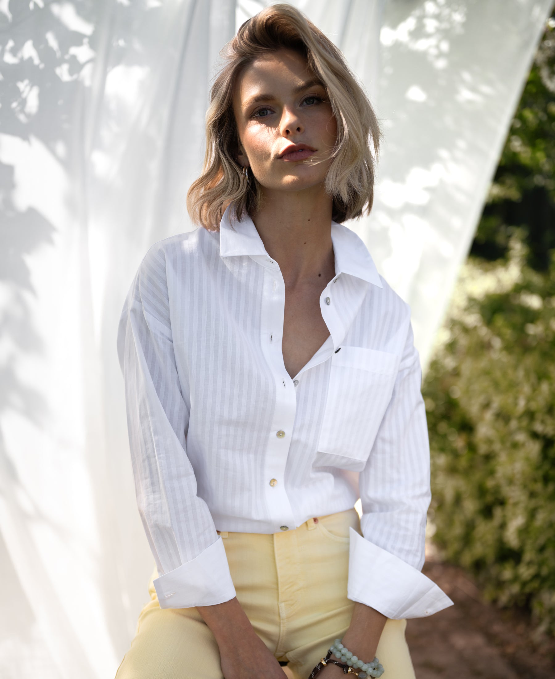 Woman wearing a white striped blouse by La Pascalle, pictured outdoors.