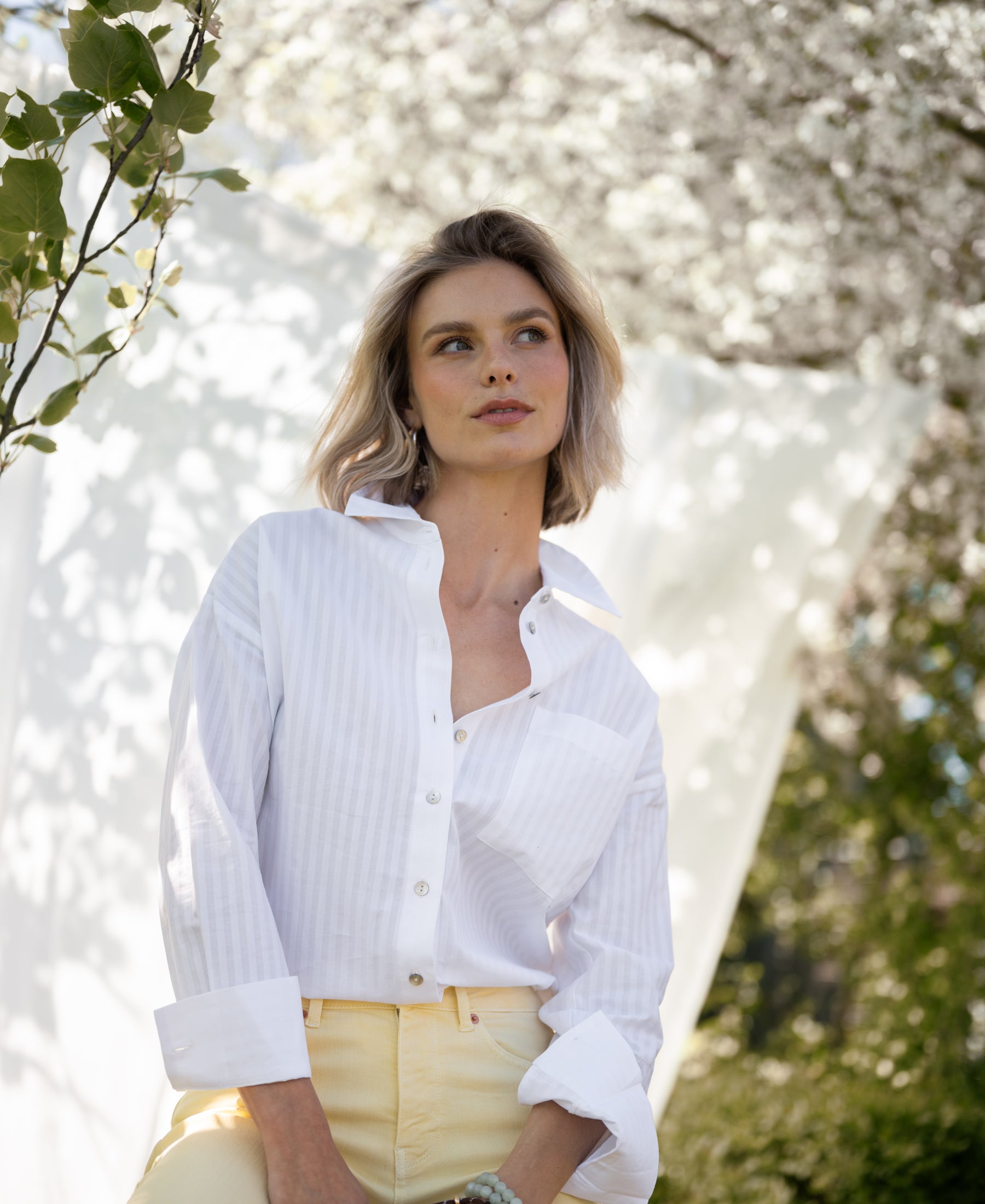 Blouse LA PASCALLE in tone-on-tone white stripes, shown outdoors among blooming trees.
