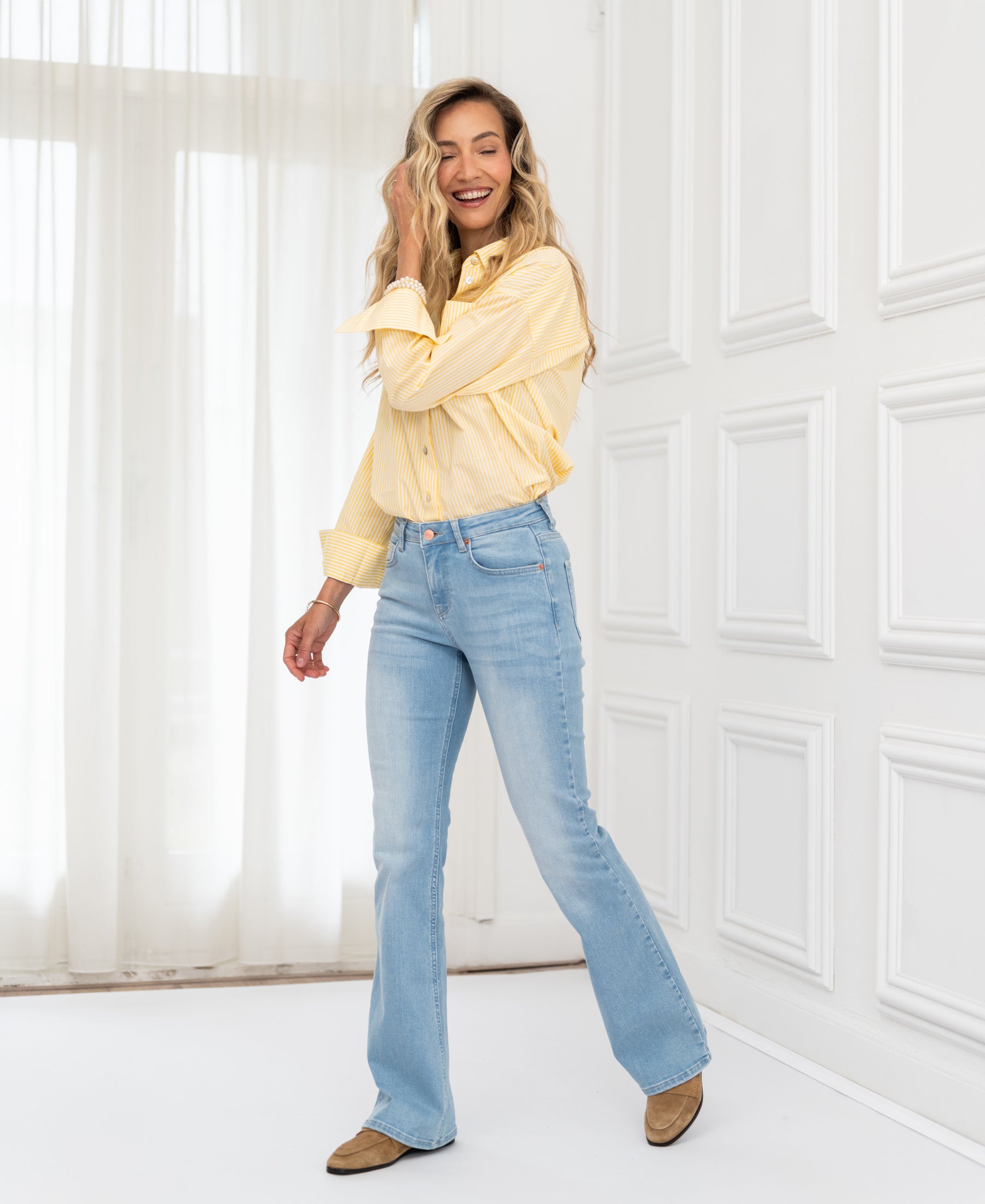 Bleached flared jeans shown in a bright room with large windows.