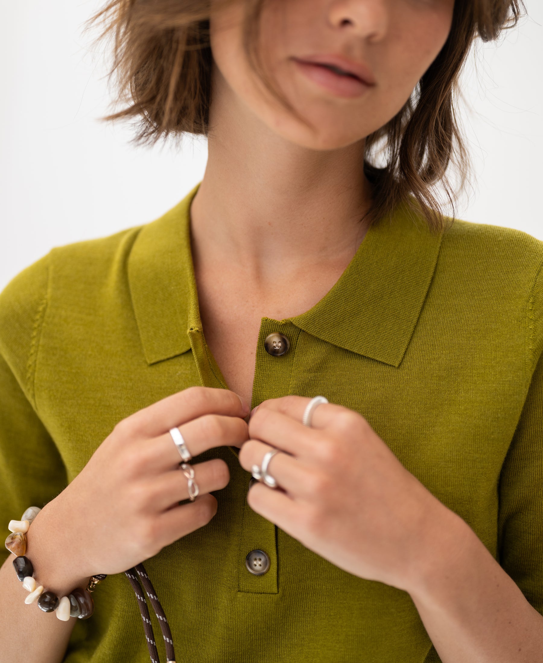 Woman wearing an olive green merino-silk polo shirt, adjusting a button.