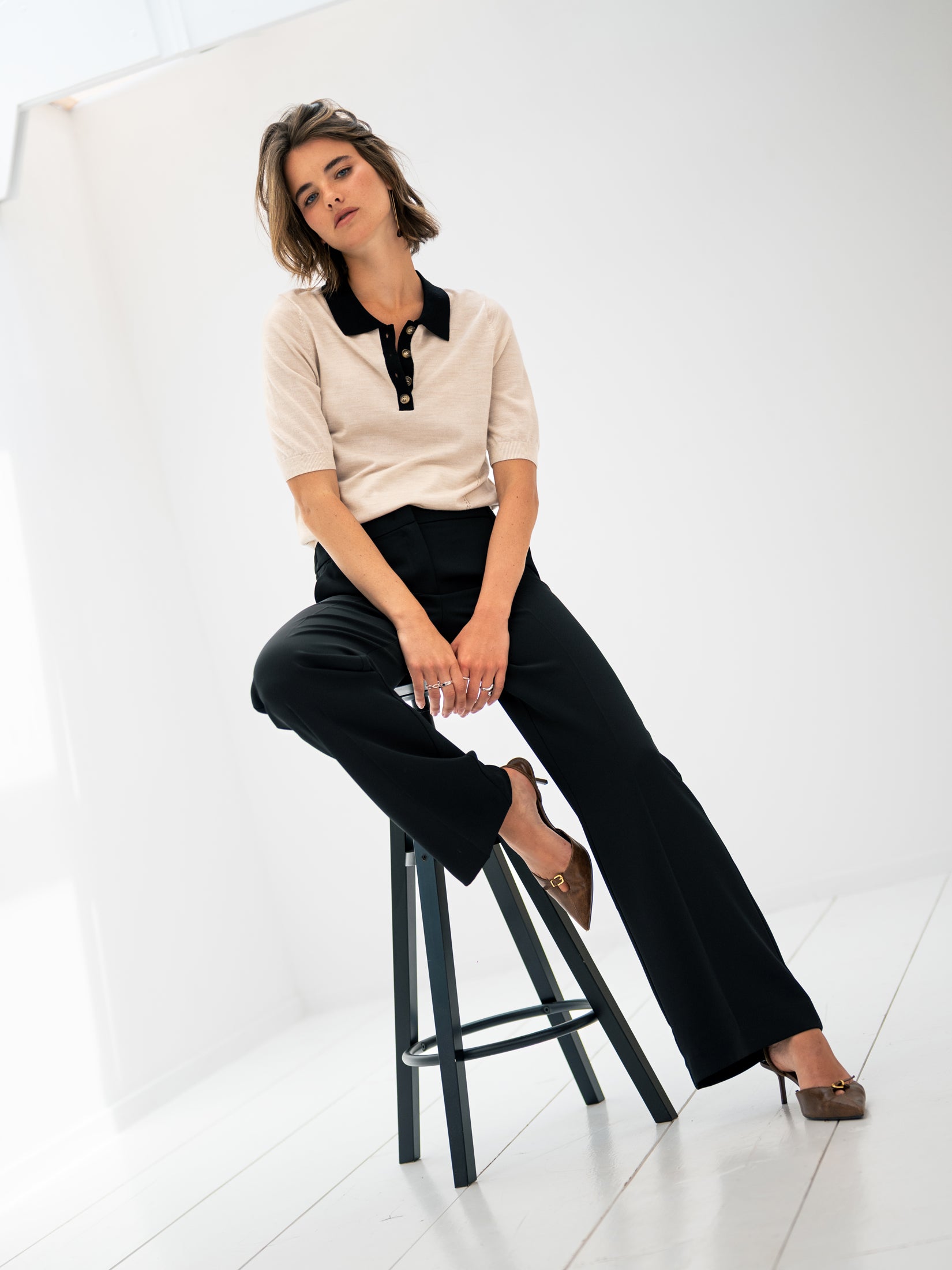 Merino wool-silk polo shirt in sand and black displayed in a minimalist room.