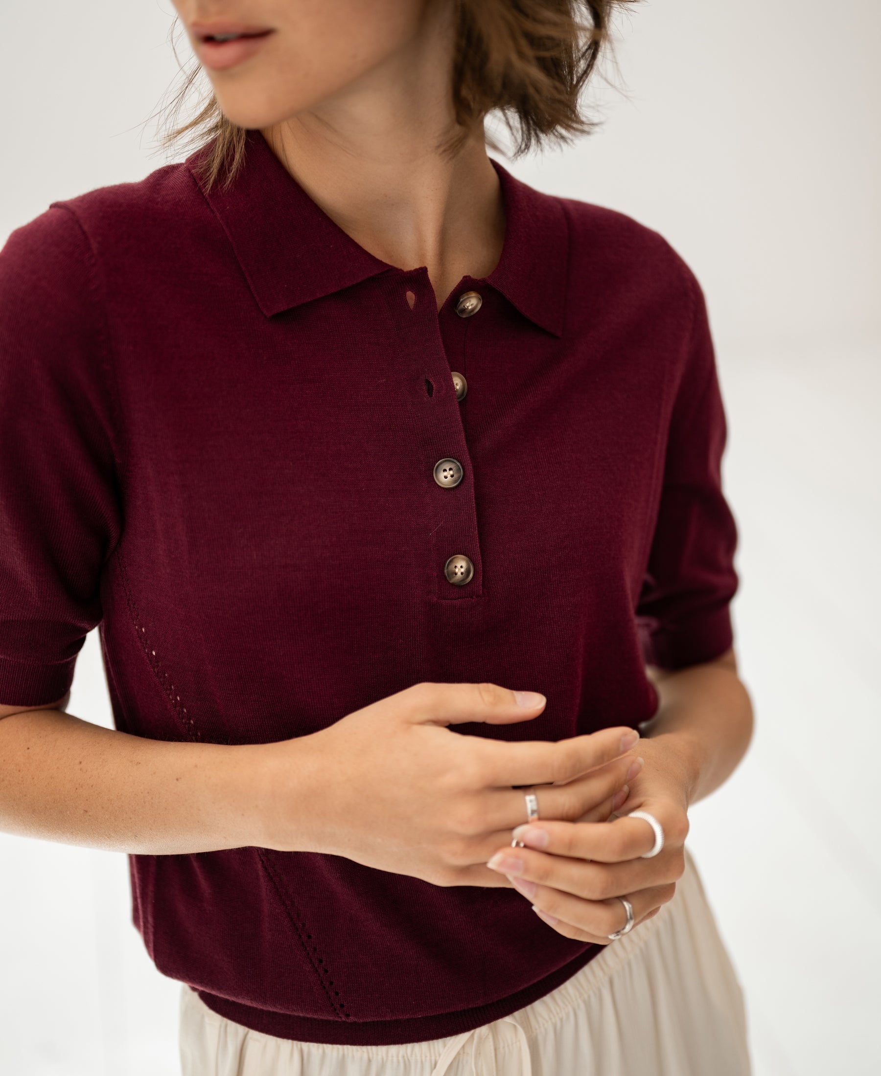 Woman wearing a merino wool and silk plum polo shirt, indoors.