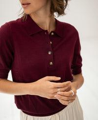 Woman wearing a merino wool and silk plum polo shirt, indoors.