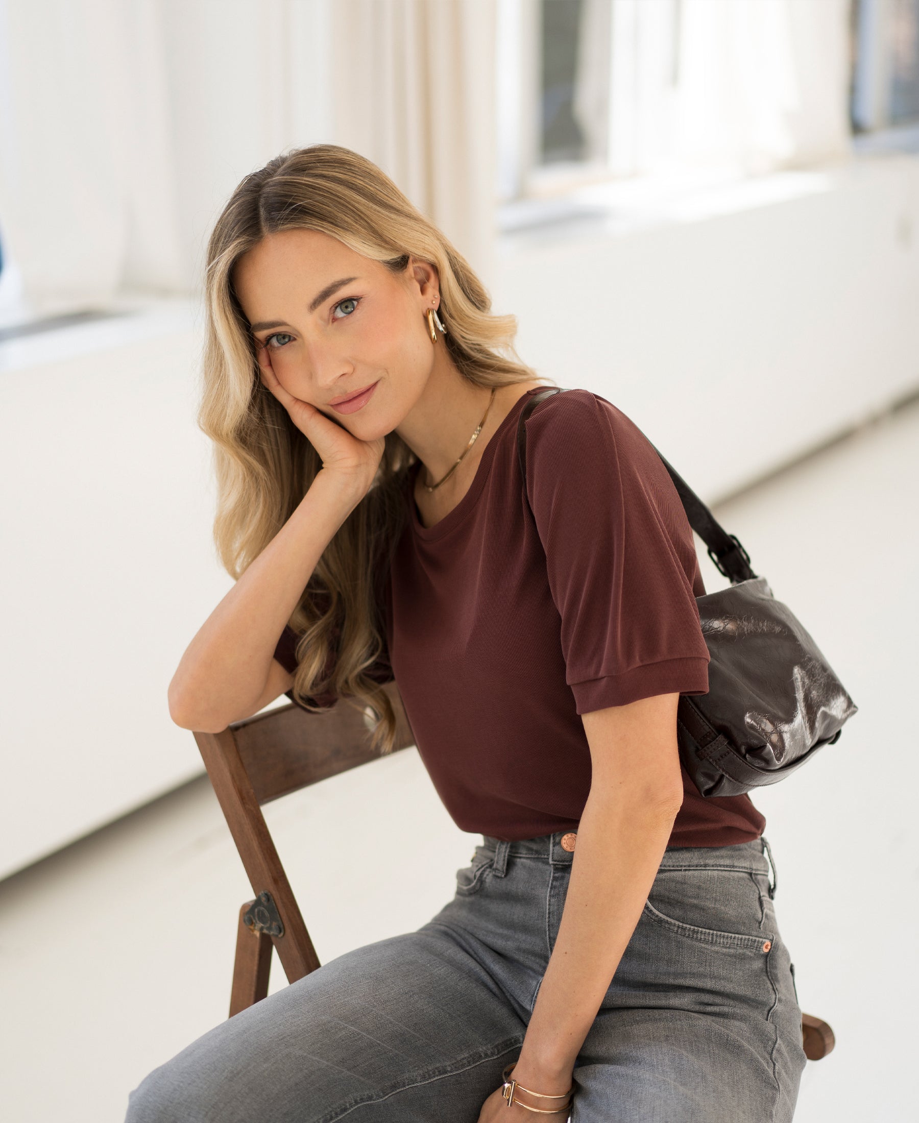 Woman wearing a Plein Publique ribbed cacao brown T-shirt, seated on a chair.