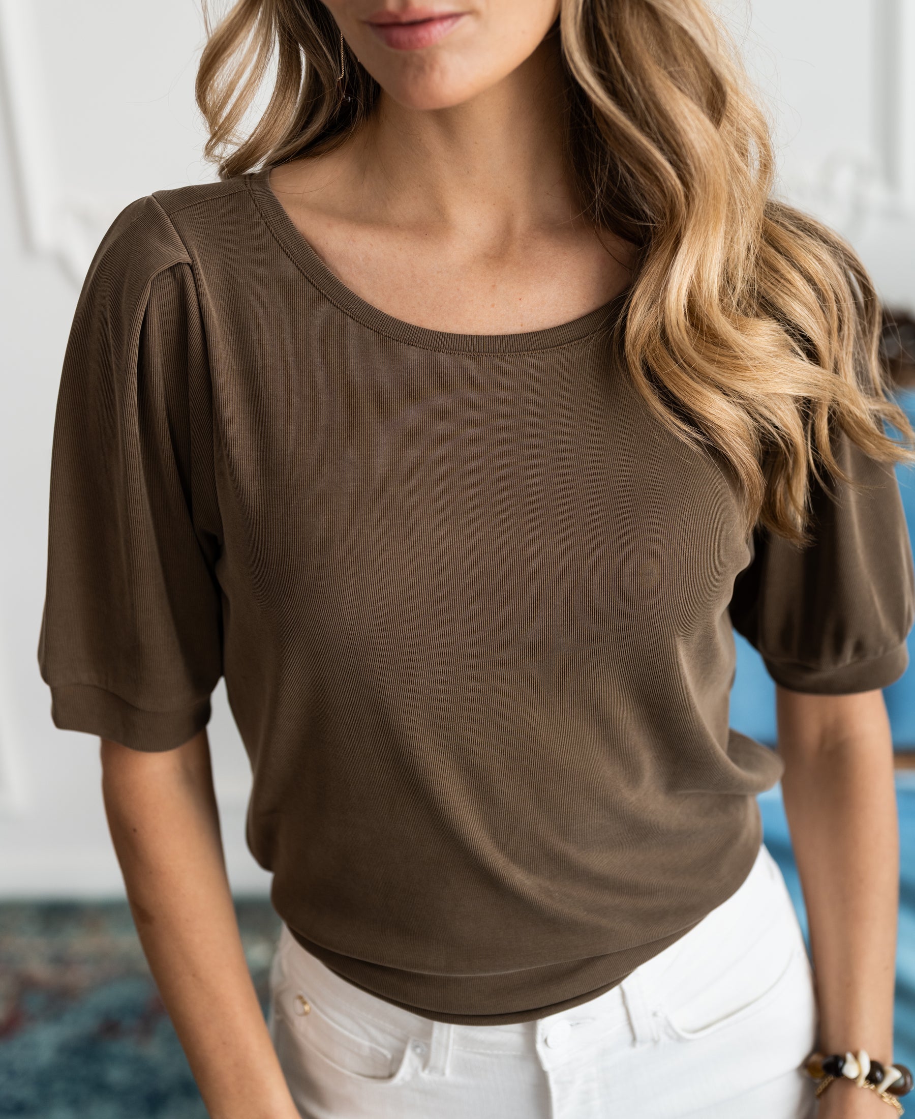 Woman wearing an army green ribbed T-shirt with wavy hair over her shoulder.