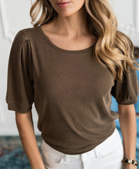 Woman wearing an army green ribbed T-shirt with wavy hair over her shoulder.