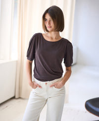 Woman wearing chocolate brown ribbed jersey T-shirt with short sleeves, hands in the shirt’s pockets.