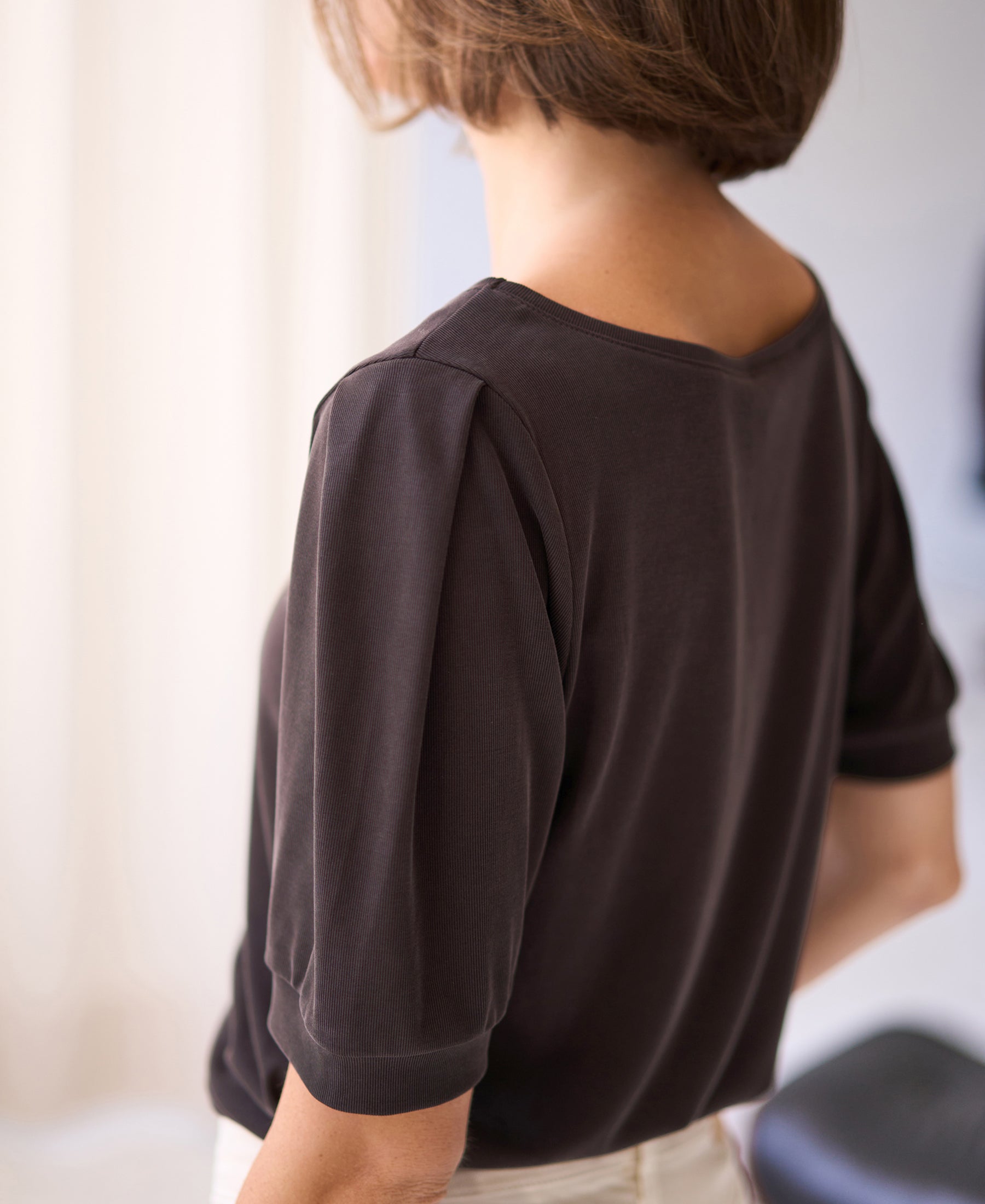 Back view of woman wearing a brown ribbed T-shirt in soft light.