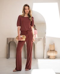 Woman wearing a ribbed henna-colored T-shirt stands in a sunlit room.