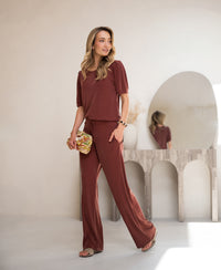 Woman wearing a ribbed henna T-shirt by Plein Publique, standing by a console table with a round mirror.