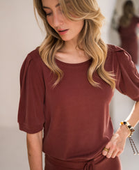 Henna ribbed T-shirt by Plein Publique, shown from the front. Model looks down; background features a blurred reflection.
