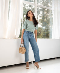 Woman indoors by windows wears a light green ribbed T-shirt from PLEIN PUBLIQUE.