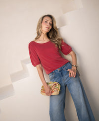 Woman wears a red ribbed T-shirt from PLEIN PUBLIQUE, standing by stairs.