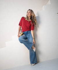 Woman wearing red ribbed T-shirt stands on white stairs, holding a purse.