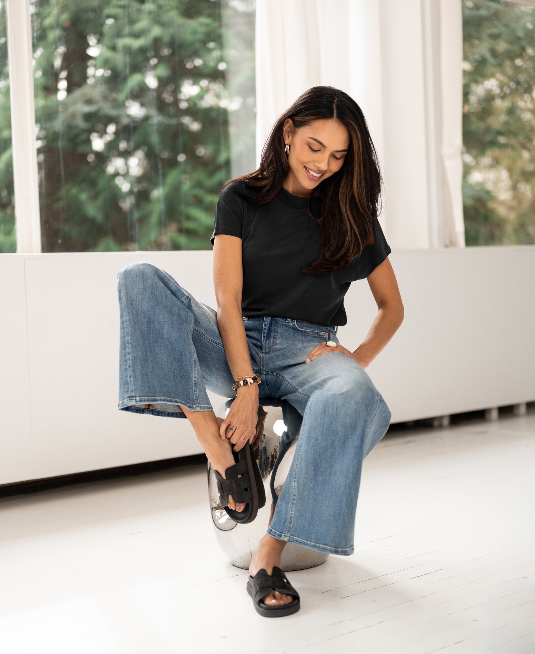 Woman wearing charcoal ribbed top sits on a chair in a bright room.