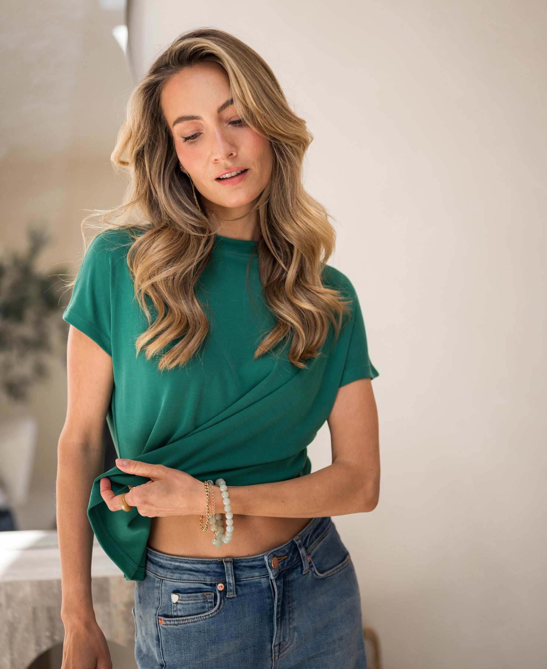 Emerald green ribbed collared top, modeled by a woman looking down and lifting the shirt.