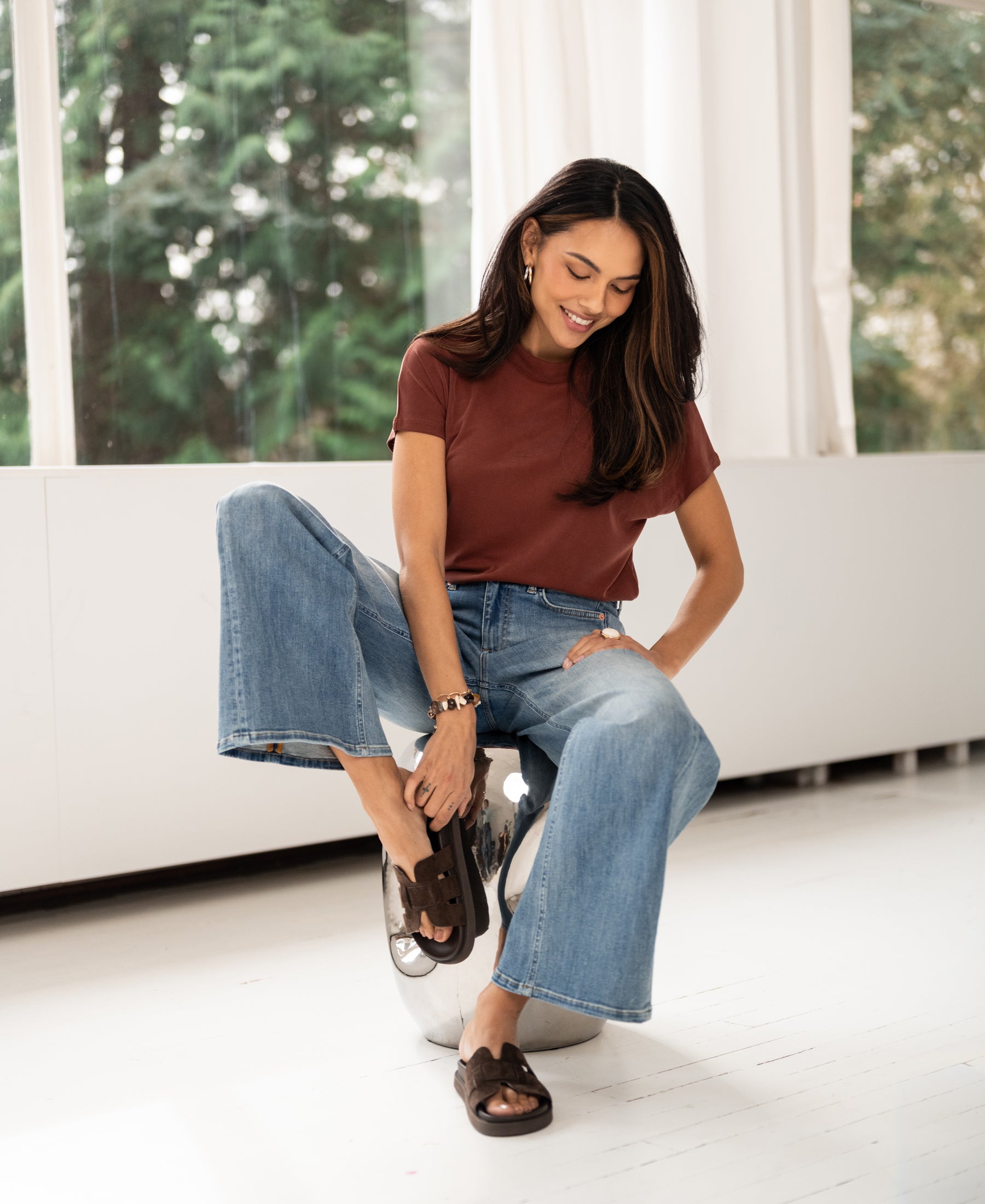 Woman wearing a ribbed henna-colored long sleeve top sits on a silver modern chair.
