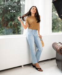 Woman in a ribbed yellow top by PLEIN PUBLIQUE, standing by a window.