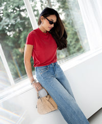 Woman wearing a red ribbed top by PLEIN PUBLIQUE near a window.